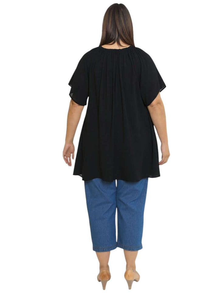 Back view of Women’s Plus Size Yasmin Top in black, featuring flutter sleeves and relaxed fit, styled with denim pants.