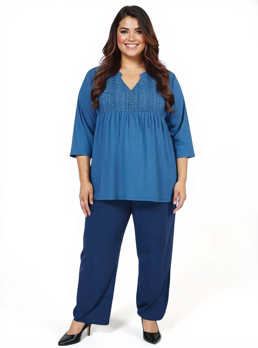Plus size woman wearing the Bellamy Top in teal, featuring a lace front bib and 3/4 sleeves, styled with navy pants.