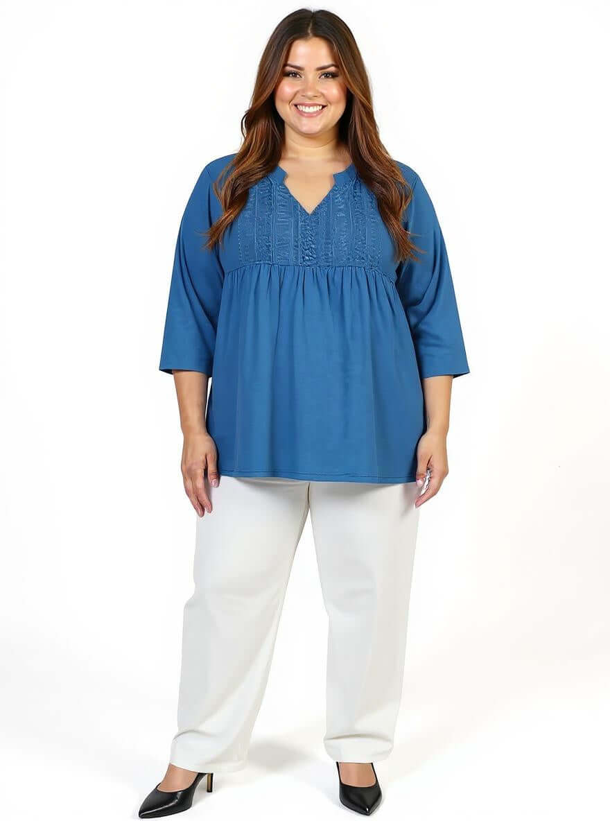 Plus size woman wearing Bellamy Top in teal with lace front bib and three-quarter sleeves, styled with light pants.