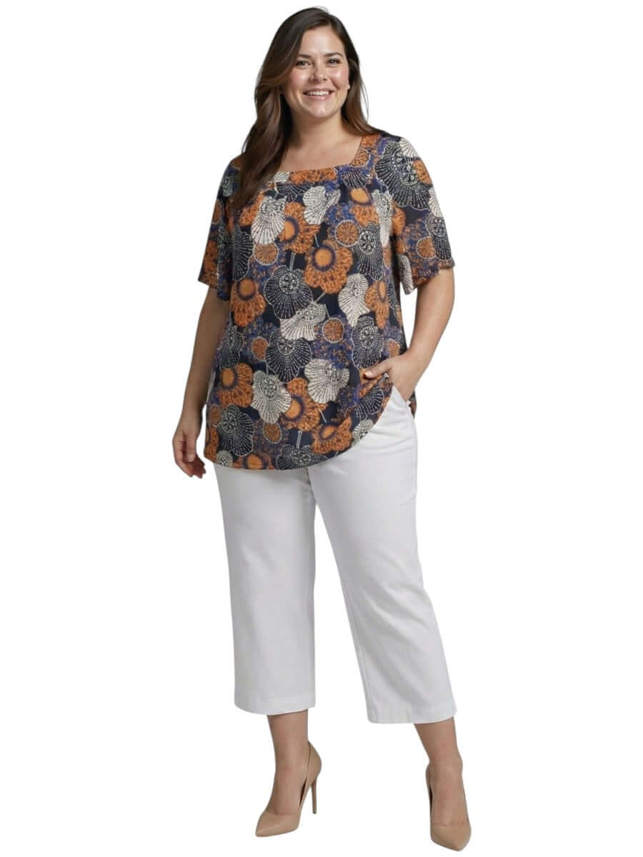 Lora Top - Navy Print worn by a plus size model featuring a floral design, paired with white pants.