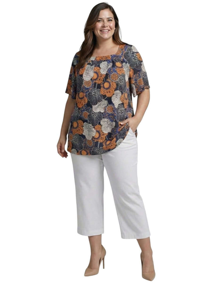 Lora Top - Navy Print worn by a plus size model featuring a floral design, paired with white pants.