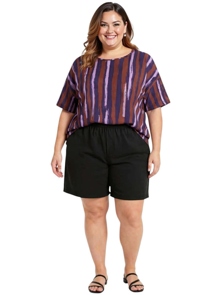 Model wearing the Velma Top - Purple Print with black shorts, showcasing women's plus size fashion.