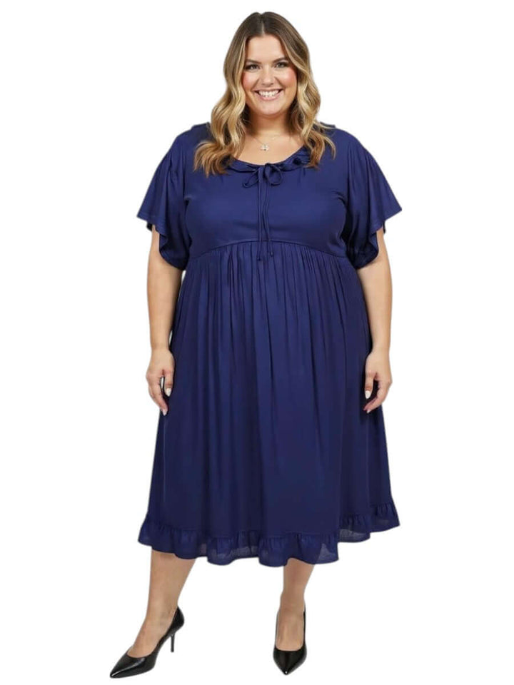 Plus size woman wearing the Dale and Waters Trinity Dress in navy, featuring a round neckline and pleated ruffle.