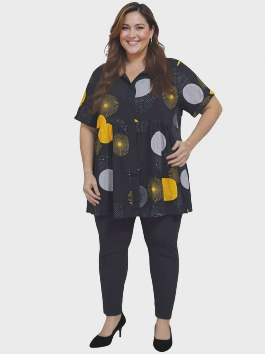 Coreen Tunic - Black Print worn by a curvy woman, featuring a black babydoll blouse with colorful patterns and button-down front.