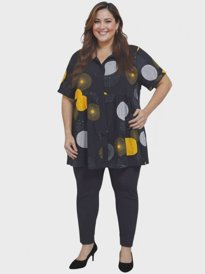 Coreen Tunic - Black Print worn by a curvy woman, featuring a black babydoll blouse with colorful patterns and button-down front.