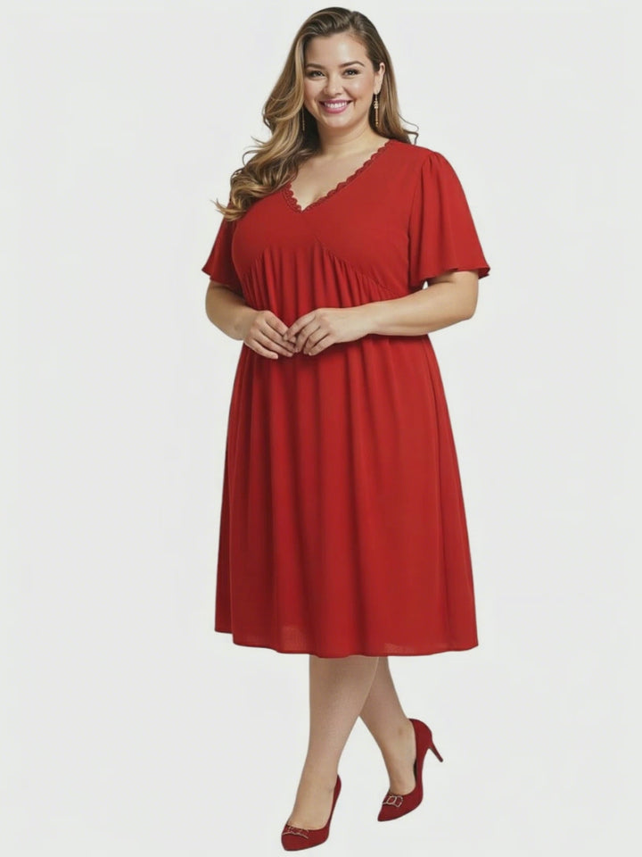 Angelica Dress - Red worn by a plus size woman, featuring flattering V-neckline and flowing polyester fabric.