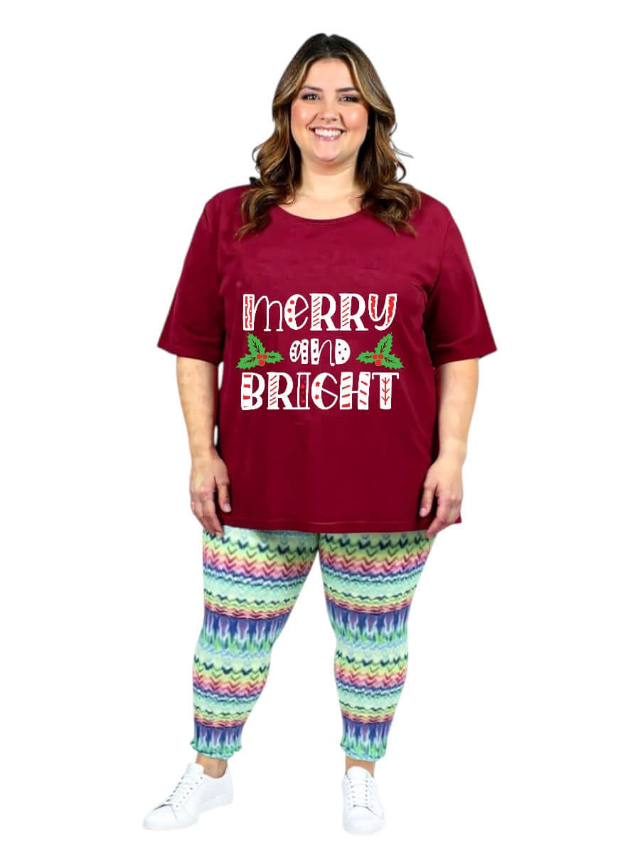 Model wearing CHRISTMAS Round Neck Tees - Cotton Polyester with 'Merry and Bright' text and colorful patterned pants.